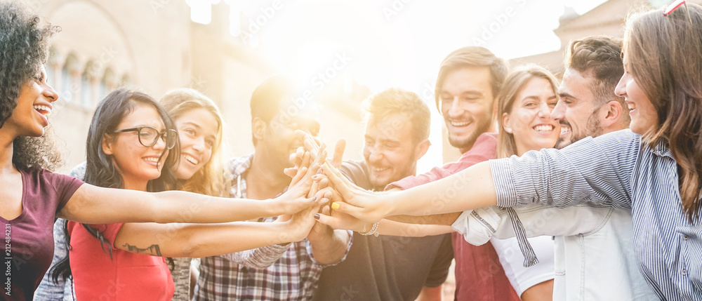 Groupe de jeunes adultes hommes et femmes souriants réunis en extérieur, tendant les bras pour une tape collective tout en se croisant les doigts, symbole d’amitié, de cohésion et d’esprit d’équipe