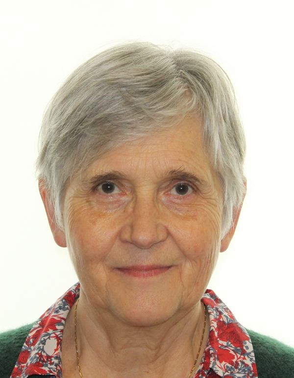 Portrait d'une femme souriante avec une rouge à lèvre distrait rose, des cheveux clair de couleur gris et une chemisier à fleur rouge en dessous d'un pull vert