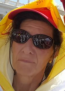Portrait d’une femme portant des lunettes de soleil, une casquette rouge et un foulard jaune, en extérieur lors d’un événement ou rassemblement sous le soleil
