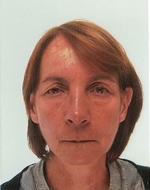 Portrait d'une femme aux cheveux courts et bruns, regardant directement la caméra avec une expression neutre, vêtue d'une chemise à rayures, sur un fond blanc.